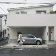 Editorial photograph of a tiny contemporary house on a narrow residential lane in Tokyo, its upper.