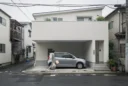 Editorial photograph of a tiny contemporary house on a narrow residential lane in Tokyo, its upper.