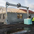 Editorial photograph of a low-rise housing construction site in Denmark, a gantry-mounted concrete printer spanning.