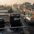 Editorial photograph from an accessible rooftop in a residential neighborhood of Mexico City, black plastic tinacos.