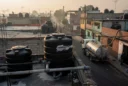 Editorial photograph from an accessible rooftop in a residential neighborhood of Mexico City, black plastic tinacos.