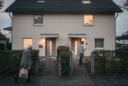Editorial photograph of an ordinary detached house in a German residential neighbourhood, adapted with two modest.