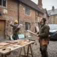 Editorial photograph of a conservation architect and a furniture maker surveying a weathered Tudor-period brick building.
