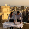 Editorial photograph conceived in Benghazi, Libya: two local urban planners on a rooftop overlooking low-rise concrete.