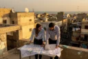 Editorial photograph conceived in Benghazi, Libya: two local urban planners on a rooftop overlooking low-rise concrete.