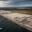 Oblique aerial editorial photograph of coastal reclamation beside a marine construction zone on southern Lolland, Denmark.