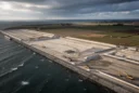 Oblique aerial editorial photograph of coastal reclamation beside a marine construction zone on southern Lolland, Denmark.