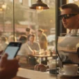 Editorial photograph inside a busy street-corner café at late afternoon: a customer wearing black Ray-Ban Meta.