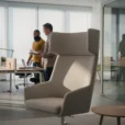 Editorial photograph inside a contemporary office furniture showroom being tested by adult users, a high-backed acoustic.