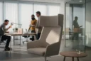 Editorial photograph inside a contemporary office furniture showroom being tested by adult users, a high-backed acoustic.