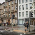 Editorial photograph of an ordinary Glasgow street where weathered sandstone tenements meet a contemporary apartment block.
