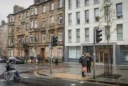 Editorial photograph of an ordinary Glasgow street where weathered sandstone tenements meet a contemporary apartment block.