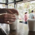 Editorial photograph inside a small Florida coffee shop at morning rush, a barista’s hands folding.
