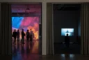 Editorial photograph inside a contemporary art museum, looking across a deep doorway between an immersive projection.