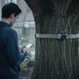 Staged editorial photograph exploring app-controlled wood-knocking: a person holding a smartphone stands several metres from.