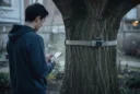 Staged editorial photograph exploring app-controlled wood-knocking: a person holding a smartphone stands several metres from.