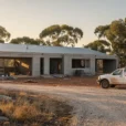 Editorial photograph of an unfinished contemporary concrete residence with a corrugated-metal roof in Australian bushland, viewed.