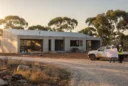 Editorial photograph of an unfinished contemporary concrete residence with a corrugated-metal roof in Australian bushland, viewed.