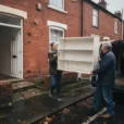 Editorial photograph of a second-hand IKEA furniture handover outside a modest terraced home in Manchester: two.