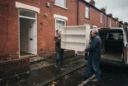 Editorial photograph of a second-hand IKEA furniture handover outside a modest terraced home in Manchester: two.