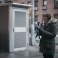 Editorial photograph of a freestanding modular public toilet on a New York City sidewalk, an adult.