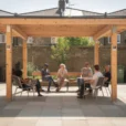 Editorial photograph of a modest timber shade structure in a community courtyard in Camden, north London.