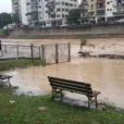 Editorial photograph of a riverside public park in a Brazilian city after heavy rain, muddy floodwater.