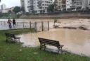 Editorial photograph of a riverside public park in a Brazilian city after heavy rain, muddy floodwater.