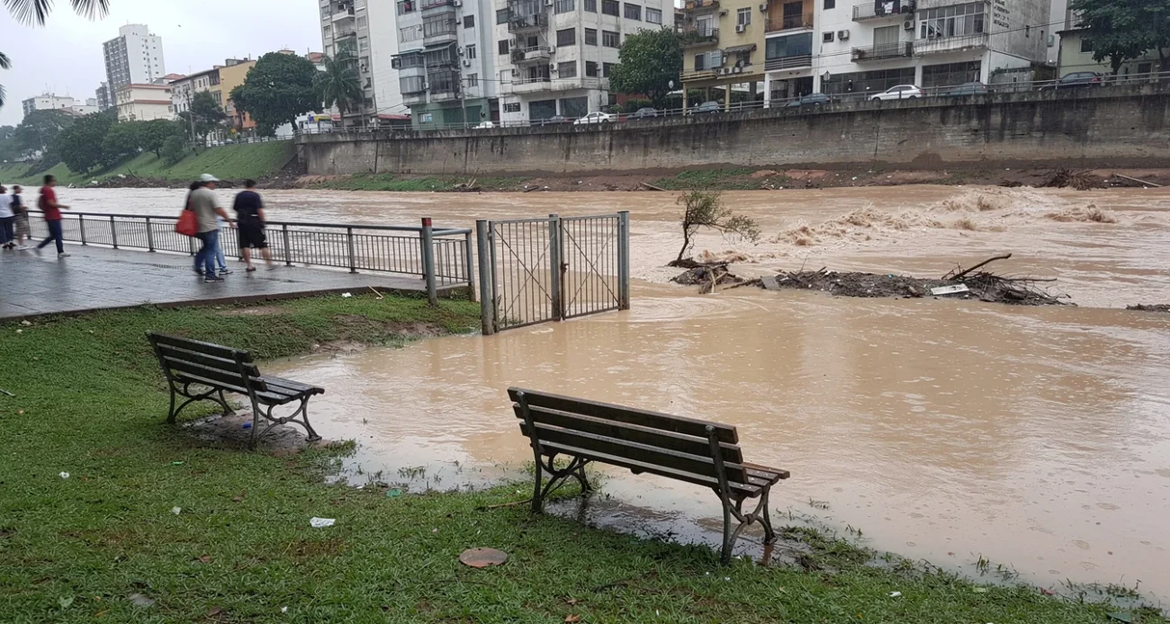 Editorial photograph of a riverside public park in a Brazilian city after heavy rain, muddy floodwater.