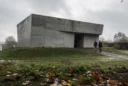 Editorial photograph of a monolithic concrete art pavilion on a grassy mound in a sculpture garden.