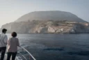 Editorial photograph from a small passenger boat approaching Sazan island, Albania, with its rugged coastline.