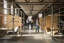 Editorial photograph of a converted warehouse workspace fitted with reused galvanized steel scaffolding, visible couplers.